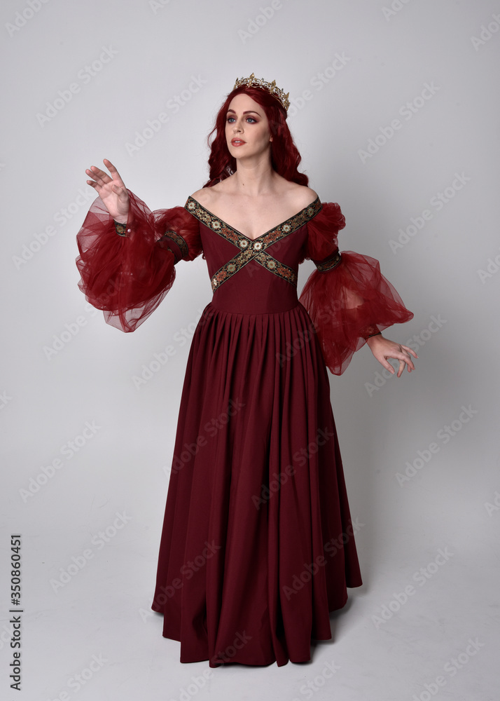 Portrait of a beautiful woman with red hair wearing a flowing Burgundy fantasy gown and golden crown. full length standing pose, isolated against a studio background
Portrait of a beautiful woman with red hair wearing a flowing Burgundy fantasy gown and golden crown. full length standing pose, isolated against a studio background