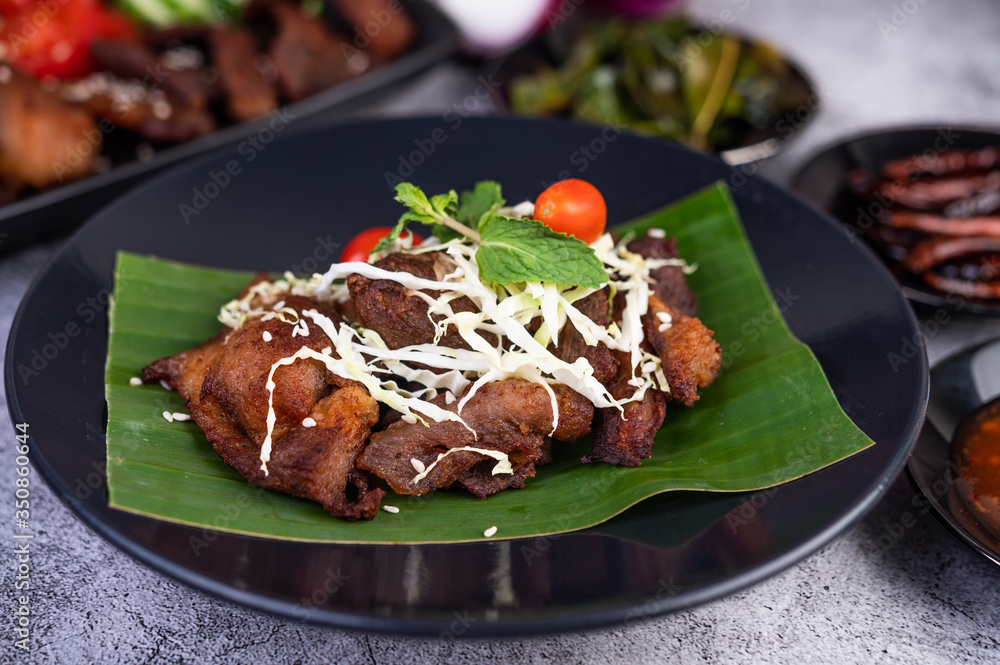 Fried pork topped with sesame seeds put on a banana leaf in a black dish. Fried pork topped with sesame seeds put on a banana leaf in a black dish.