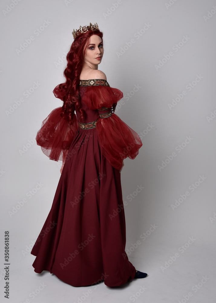Portrait of a beautiful woman with red hair wearing a flowing Burgundy fantasy gown and golden crown. full length standing pose, isolated against a studio background
Portrait of a beautiful woman with red hair wearing a flowing Burgundy fantasy gown and golden crown. full length standing pose, isolated against a studio background