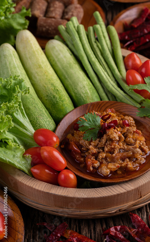 Sweet pork in a wooden bowl with cucumber, long beans, tomatoes, and side dishes.