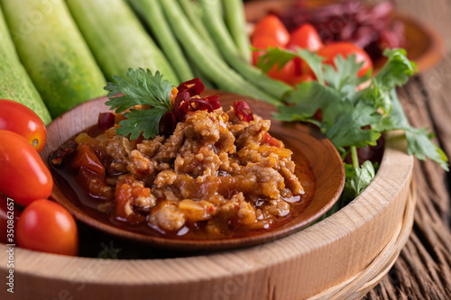 Sweet pork in a wooden bowl with cucumber, long beans, tomatoes, and side dishes.