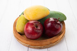 Apples and mangoes in a wooden tray.