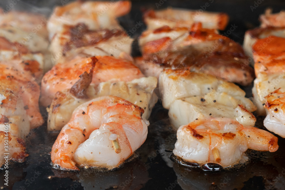 Shrimps and salmon cooking on black barbecue background