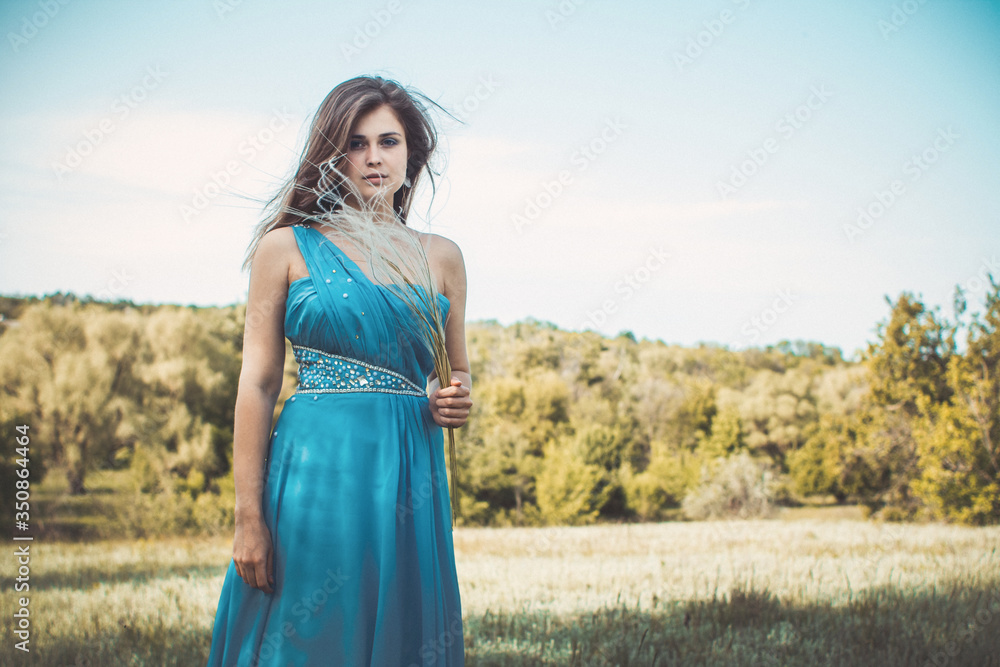 beautiful romantic girl enjoying nature with fluffy feather grass in hands, young elegant woman face, bride in blue long dress on the background of landscape beautiful romantic girl enjoying nature with fluffy feather grass in hands, young elegant woman face, bride in blue long dress on the background of landscape