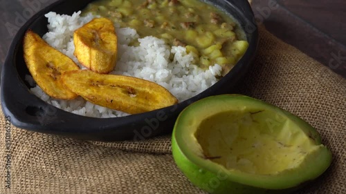 Artisanal rustic dish containing meat hash with rice and slices of fried plantains and an avocado rotating on a jute mat 