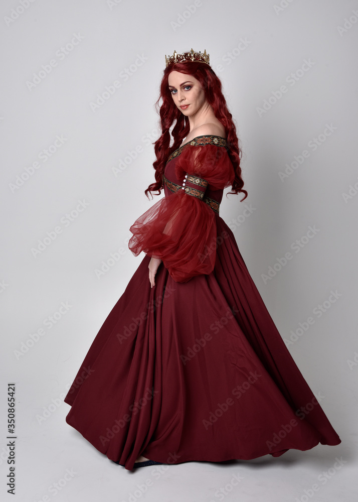 Portrait of a beautiful woman with red hair wearing a flowing Burgundy fantasy gown and golden crown. full length standing pose, isolated against a studio background
Portrait of a beautiful woman with red hair wearing a flowing Burgundy fantasy gown and golden crown. full length standing pose, isolated against a studio background