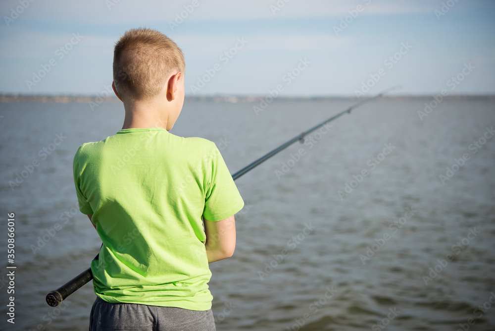 Boy fishing on a lake in the summer. View from back