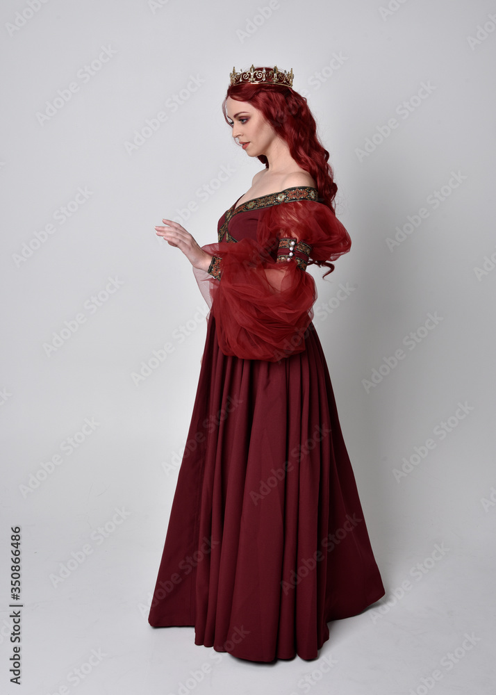 Portrait of a beautiful woman with red hair wearing a flowing Burgundy fantasy gown and golden crown. full length standing pose, isolated against a studio background
Portrait of a beautiful woman with red hair wearing a flowing Burgundy fantasy gown and golden crown. full length standing pose, isolated against a studio background