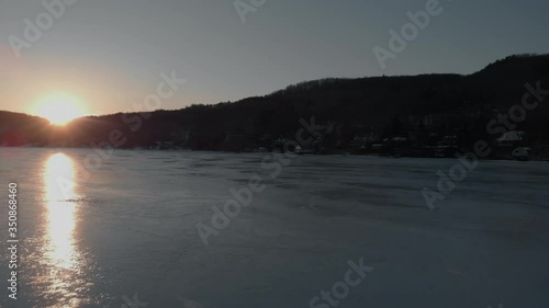 Canadian Flag Stands On A Frozen Lake And Waving In The Wind Near The North Hatley In Quebec, Canada, With The Dramatic Sunset In The Background. - aerial drone shot photo