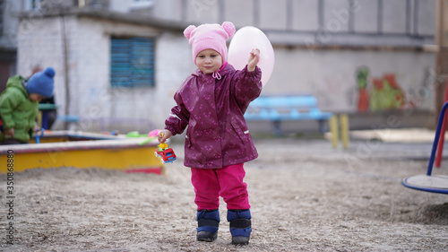 Portrait of cute little girl in pink hat with pompons on playground