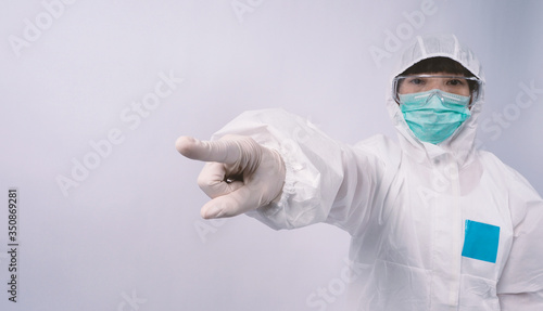 Doctor in PPE suit or Personal Protection Equipment point out to copy space and wearing white color medical rubber gloves and clear goggles glasses and green N95 mask to protect pandemic virus