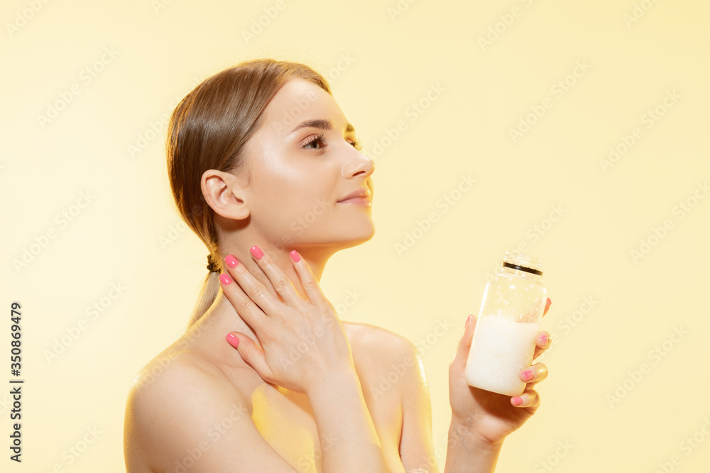 Close up of beautiful young woman massaging skin with moisturizer yellow background. Concept of cosmetics, makeup, natural and eco treatment, skin care. Shiny and healthy skin, fashion, healthcare. Close up of beautiful young woman massaging skin with moisturizer yellow background. Concept of cosmetics, makeup, natural and eco treatment, skin care. Shiny and healthy skin, fashion, healthcare.