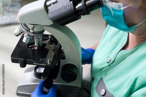 The laboratory assistant is looking through a microscope. Laboratory technician in blue mittens