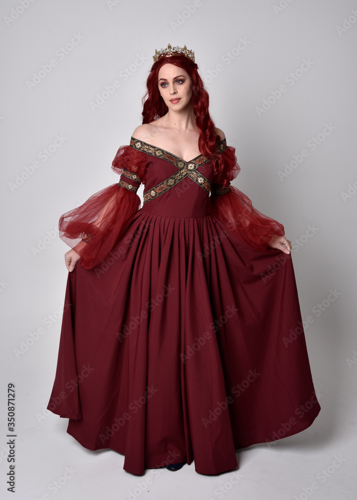 Portrait of a beautiful woman with red hair wearing a flowing Burgundy fantasy gown and golden crown. full length standing pose, isolated against a studio background
Portrait of a beautiful woman with red hair wearing a flowing Burgundy fantasy gown and golden crown. full length standing pose, isolated against a studio background