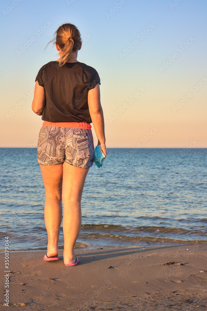 Mujer a la orilla del mar mirando el horizonte con la esperanza de terminar el confinamiento por el virus del COVID-19 Mujer a la orilla del mar mirando el horizonte con la esperanza de terminar el confinamiento por el virus del COVID-19