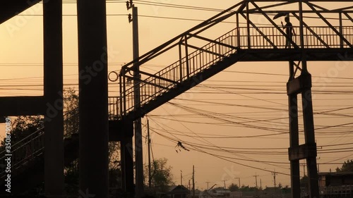 Silhouette of man is holding umbrella crossing the overpass.