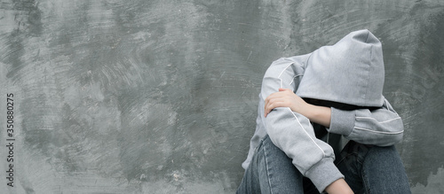 Depressed and hopeless teenage girl sitting alone after using drugs or drunk alcohol over grunge concrete wall. Drugs addiction and withdrawal symptoms concept. International Day against Drug Abuse.