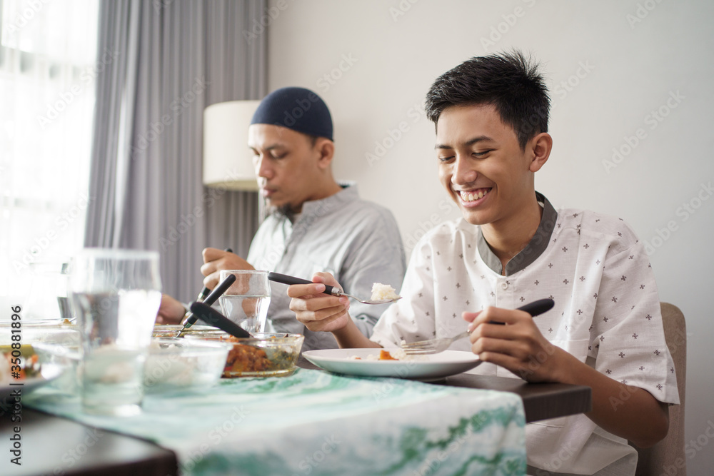 muslim father and son eating some dinner together at home muslim father and son eating some dinner together at home