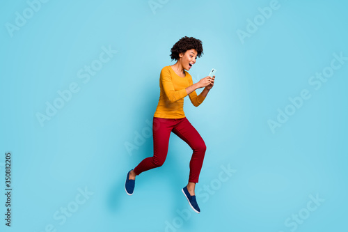 Full length body size view of her she nice attractive positive glad cheerful cheery wavy-haired girl jumping running using cell having fun isolated on bright vivid shine vibrant blue color background