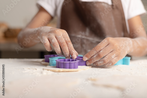 A little girl is wearing a brown apron using a purple mold to cut the dough