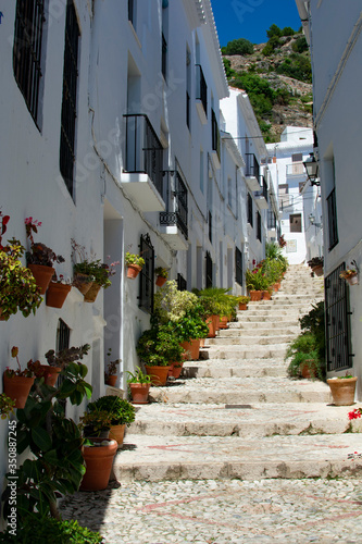 A view of a narrow, steep alley in the amiable, pretty small white town of Frigiliana, in Andalusia, southern Spain. Picturesque scenery with beautiful flowers decorating the setting.