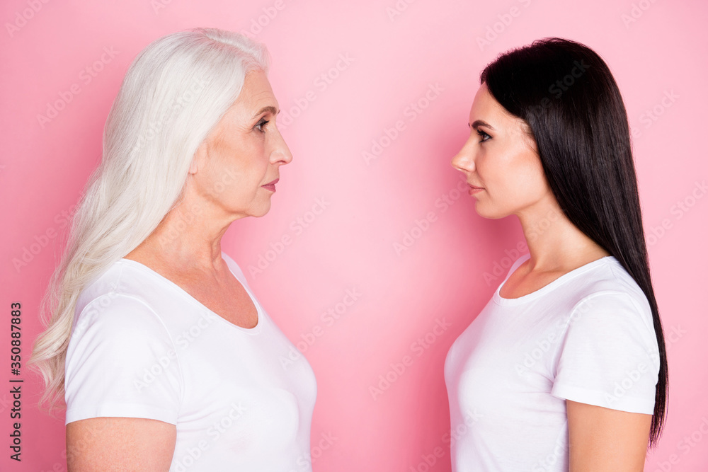 Profile photo of pretty old mother young daughter two ladies standing opposite look eyes see age difference wisdom wear casual white t-shirts isolated pastel pink color background Profile photo of pretty old mother young daughter two ladies standing opposite look eyes see age difference wisdom wear casual white t-shirts isolated pastel pink color background