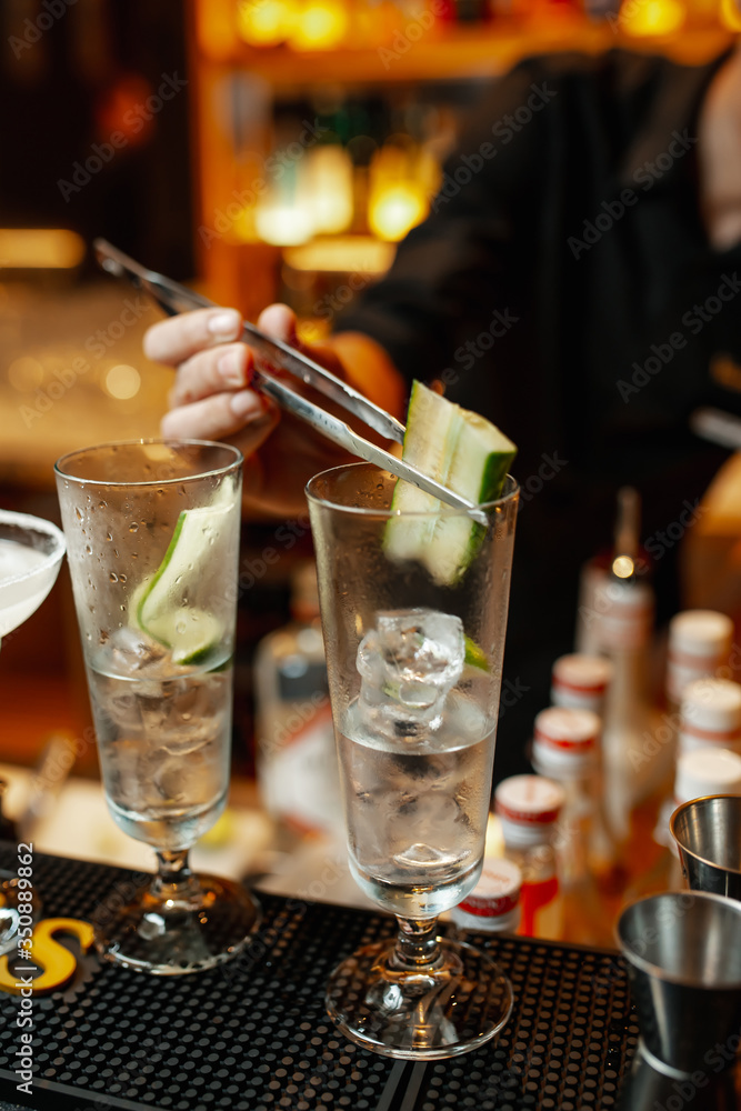 Bartender decorates cocktail with cucumber slice using tweezers.  Close-up on hands