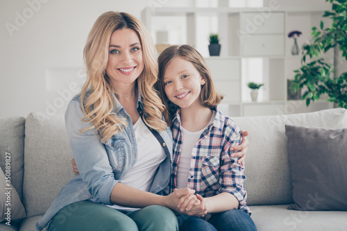 Photo of domestic charming blond lady mommy daughter sitting comfy couch hold arms stay home quarantine spend weekend together hugging best friends living room indoors