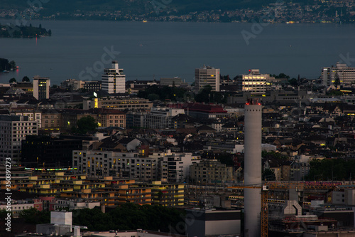 Zurich city Switzerland view with tall concrete illuminated chimney from famous vista point in the evening blue hour evening after sunset cloudy sky