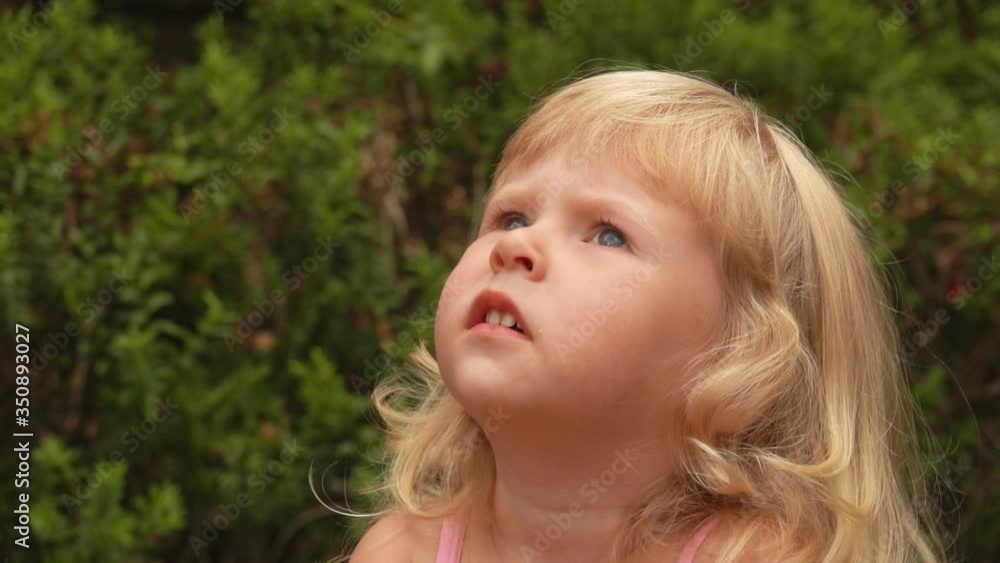 Beautiful little blond girl is smiling and looking at the sky in sunny park outdoors Beautiful little blond girl is smiling and looking at the sky in sunny park outdoors