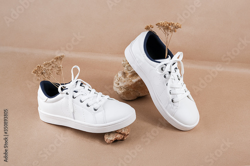 Ethical vegan shoes concept. A pair of white sneakers with dry flowers on the stones against a background of neutral beige craft paper