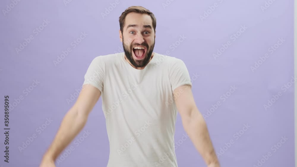 A positive happy young man wearing white t-shirt is doing a winner gesture while standing isolated over gray background A positive happy young man wearing white t-shirt is doing a winner gesture while standing isolated over gray background
