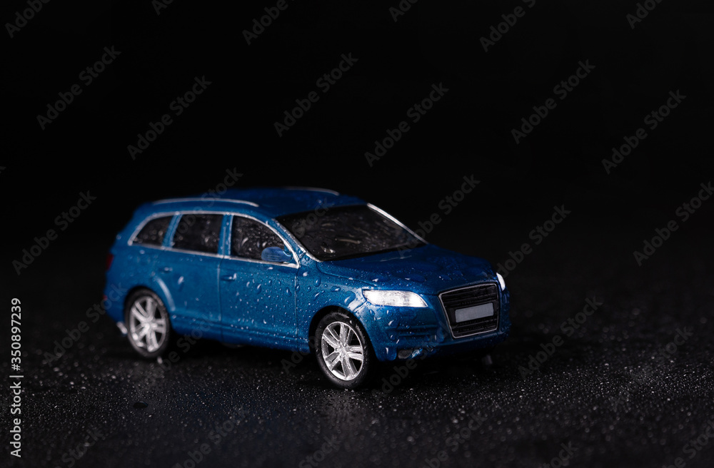 Blue  toy car with water drops on a black background. SUV car. 