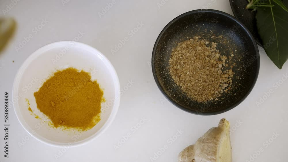 Turmeric powder poured in a white bowl next to a black bowl containing crushed coriander seeds. Top down view of a kitchen bench top. 4K pro res.
