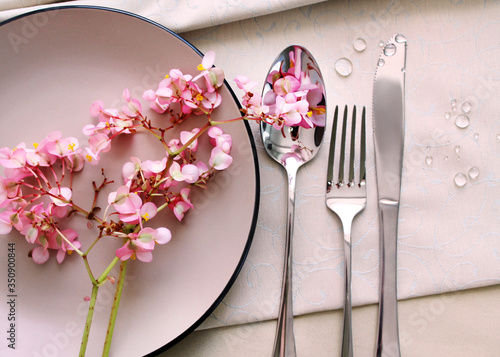 

cutlery on a serving table, close up. pink begonia flowers on a plate as a table decor. table setting details.