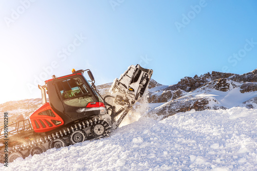 Red modern snowcat ratrack with snowplow snow grooming machine preparing ski slope piste hill at alpine skiing winter resort Ischgl in Austria. Heavy machinery mountain equipment track vehicle