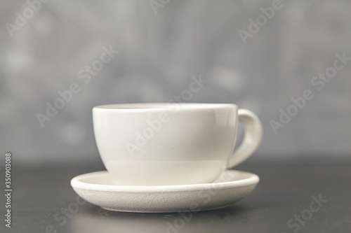 A white cup on the black table. On gray background