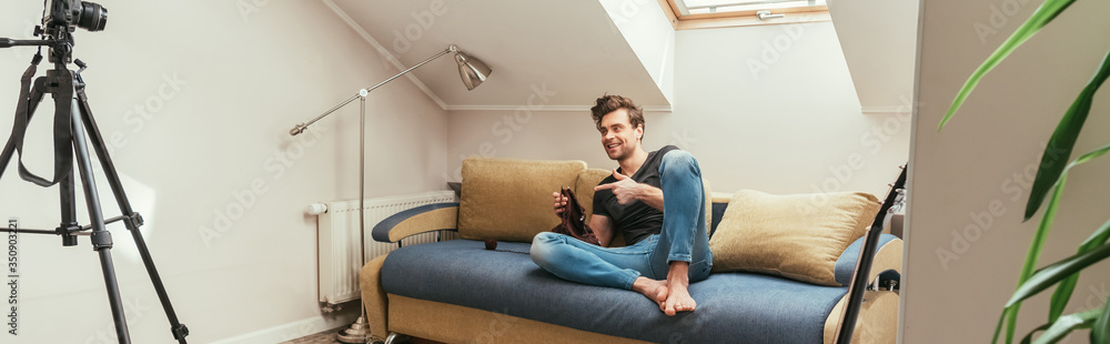 handsome vlogger pointing with finger while knitting on sofa at home in attic room, horizontal image