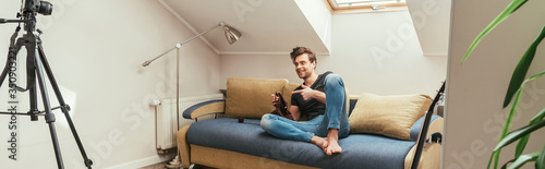 handsome vlogger pointing with finger while knitting on sofa at home in attic room, horizontal image © LIGHTFIELD STUDIOS