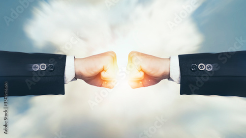 Fight, Interruption and coping with economic conflicts, competition with business competitors during the covid-19. Two fists hitting with sunlight effect on sky background. Concept of struggle. photo