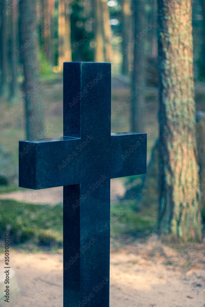 Beautiful black marble cross on a blurry forest background. Stone Orthodox cross. Selective focus on the cross. Horizontal.