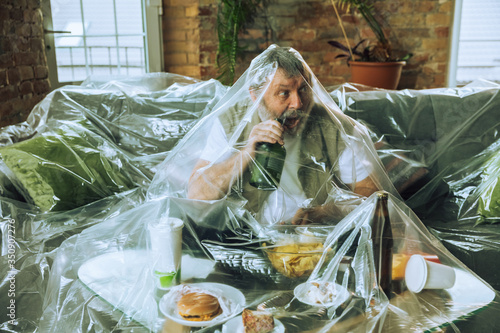 Senior man covered with plastic, eating fast food - environmental pollution by people concept. Eco campaign. We've polluted the planet so much that no longer notice it. Unhealthy, garbage, problem. photo