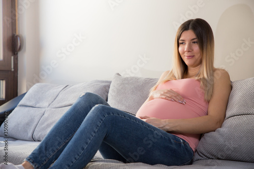 Beautiful pregnant girl sitting on the couch at home. Young pregnant woman resting on the couch.