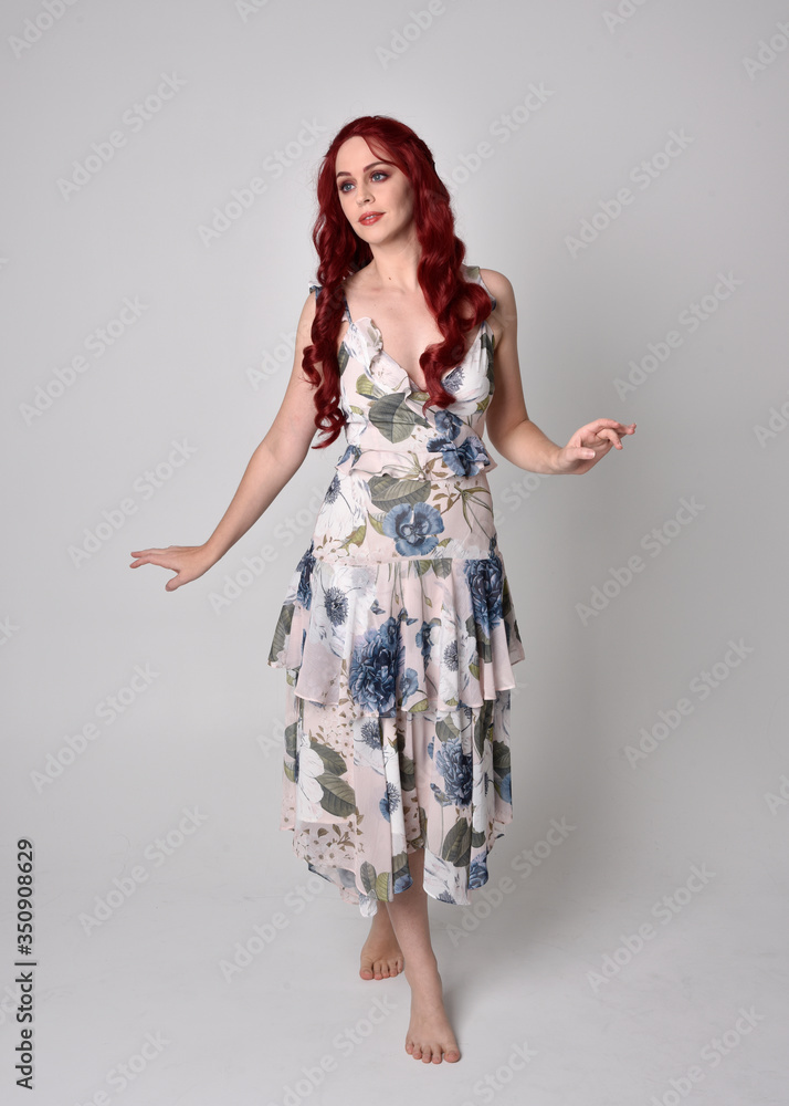Portrait of a beautiful woman with red hair wearing a flowing floral gown. full length standing pose, isolated against a studio background Portrait of a beautiful woman with red hair wearing a flowing floral gown. full length standing pose, isolated against a studio background