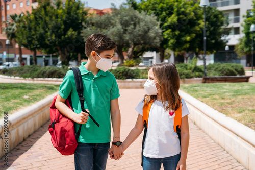 Boy and girl with backpacks and masks going to school in coronavirus pandemic