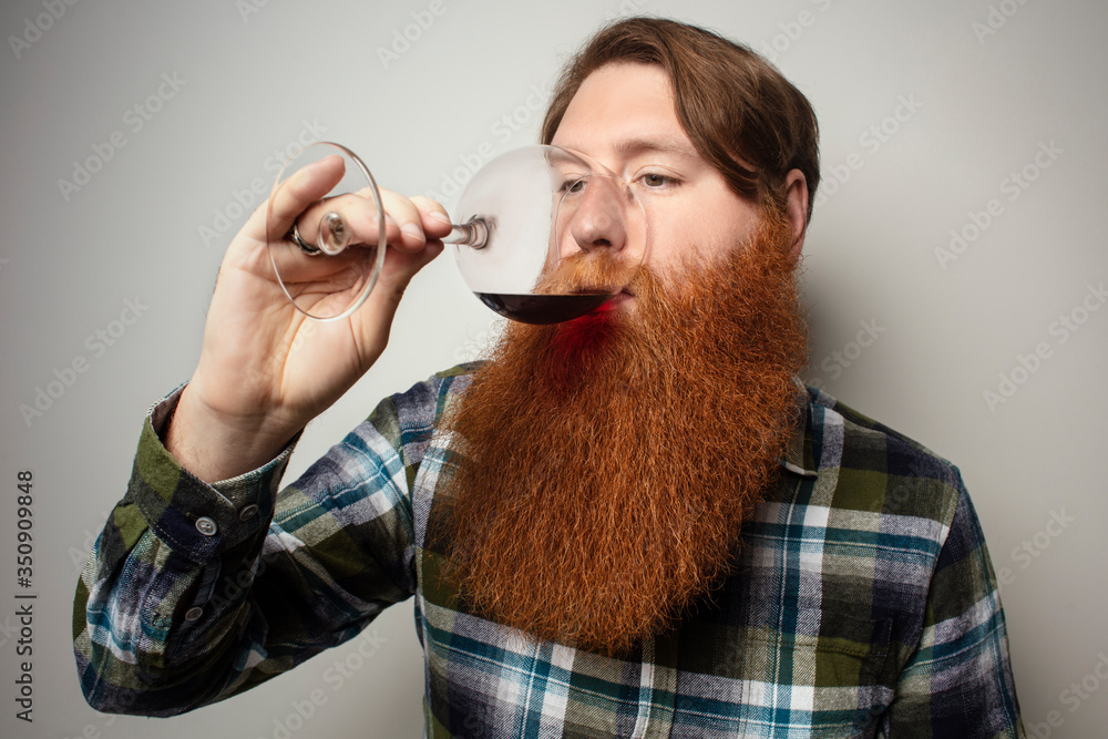 A red-bearded man drinking wine from a large glass. A vine tasting at home. Sommelier for yourself at home. A man with a big beautiful beard. A red-bearded man drinking wine from a large glass. A vine tasting at home. Sommelier for yourself at home. A man with a big beautiful beard.