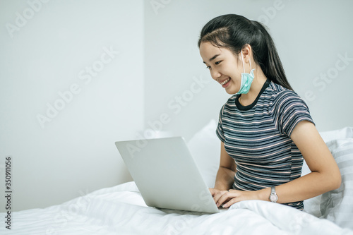 A woman wearing a striped shirt on the bed and playing laptop happily.