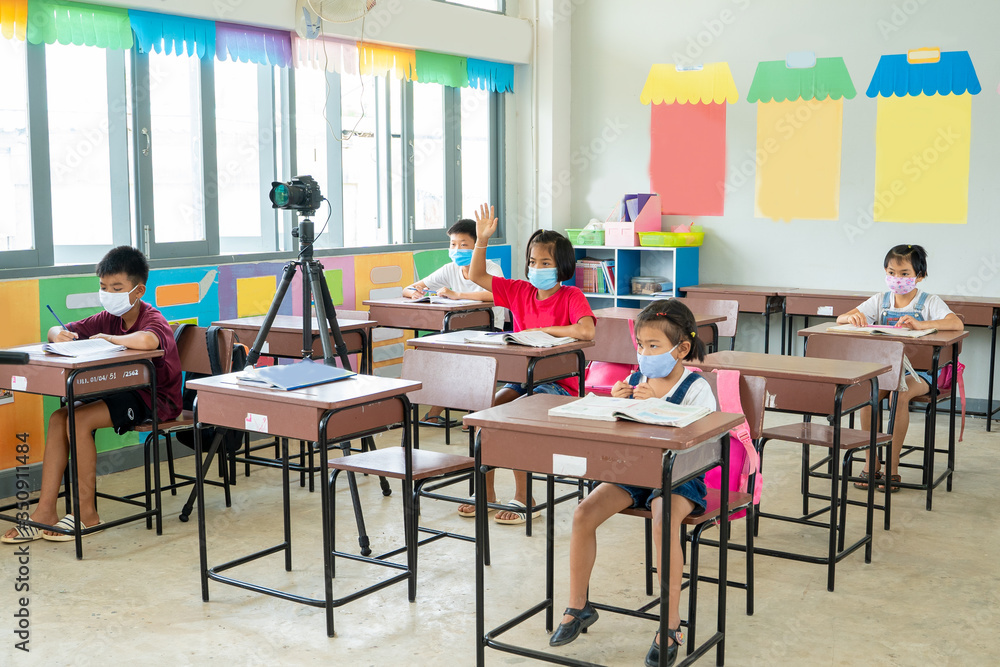 Group of school kids wearing protective mask to Protect Against Covid-19 with teacher sitting in classroom,education,elementary school,Social Distancing,learning and people concept. Group of school kids wearing protective mask to Protect Against Covid-19 with teacher sitting in classroom,education,elementary school,Social Distancing,learning and people concept.