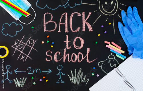 Back to school background written by crayons on the blackboard also with face mask and latex gloves to protect from coronavirus.
