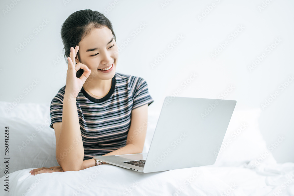 A woman wearing a striped shirt on the bed and playing laptop happily. A woman wearing a striped shirt on the bed and playing laptop happily.